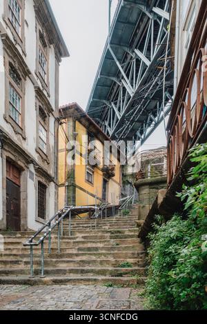 Passi di pietra si snodano attraverso lo storico quartiere di Porto Ribeira sotto l'iconica struttura del ponte Dom Luis I. Architettura portoghese e strade ripide Foto Stock