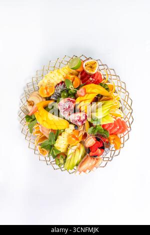 Vista dall'alto di un vivace piatto di frutta con ananas, mango, pompelmo e menta. Presentazione elegante su uno sfondo bianco pulito. Foto Stock