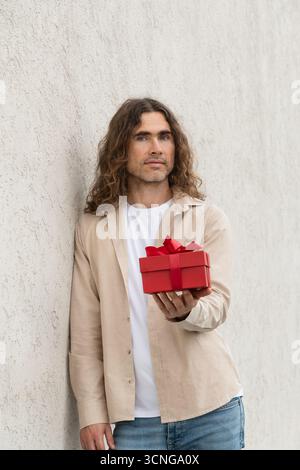 Giovane attraente che regala una confezione regalo rossa con amore. Compleanno. Sorpresa romantica e festa. Biglietto di auguri di San Valentino. Foto Stock