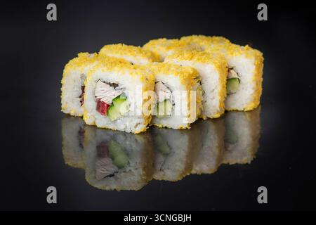 Rotoli di sushi disposti ordinatamente su una superficie nera riflettente. I panini sono ricoperti da uno strato dorato croccante e contengono cetriolo e pesce. Foto Stock