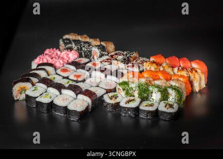 Una varietà di sushi roll disposti su una superficie nera. Comprende maki, nigiri e panini speciali con guarnizioni colorate e decorazioni. Foto Stock