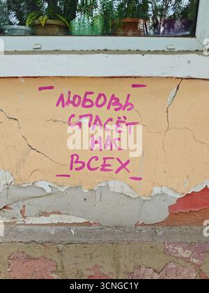 Graffiti di strada su un vecchio muro incrinato: L'iscrizione "ЛЮБОВЬ СПАСЁТ НАС ВСЕХ" (l'amore ci salverà tutti) in rosa. Una fotografia che riflette la vita urbana, Foto Stock