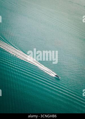 Un piccolo motoscafo attraversa il mare turchese, lasciando un sentiero bianco e spumeggiante sulla tranquilla superficie d'acqua Foto Stock