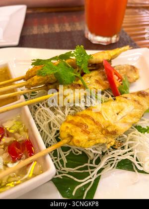 Spiedini di pollo grigliati su bastoncini di bambù con salsa ed erbe aromatiche. Servito su foglie di banana e spaghetti di riso. Foto Stock