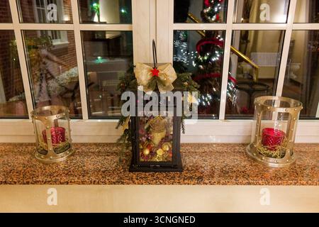 Su un'ampia soglia, tre candele. Due bicchieri di vetro sono seduti in anelli di fieno, e una terza riposa in una piccola scatola di lanterne rivestita con archi, ornamenti, A. Foto Stock