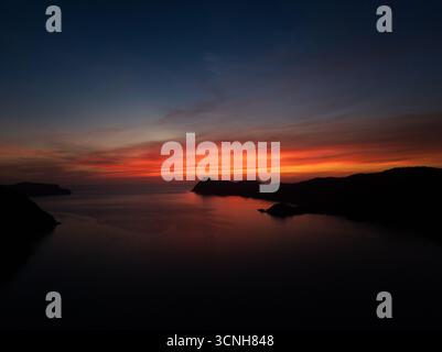 Splendido tramonto che crea una vista estetica in una combinazione di colori rosso, giallo, arancione e motivi che si affacciano sull'oceano, tranquillo e tranquillo Foto Stock
