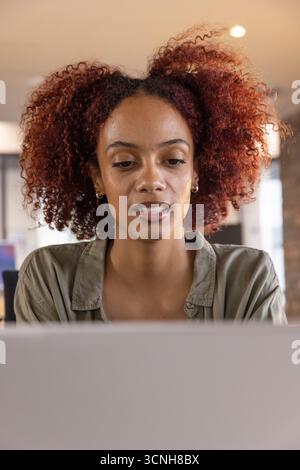 Donna afroamericana che lavora su un computer portatile alla scrivania in un moderno ufficio con finestre Foto Stock