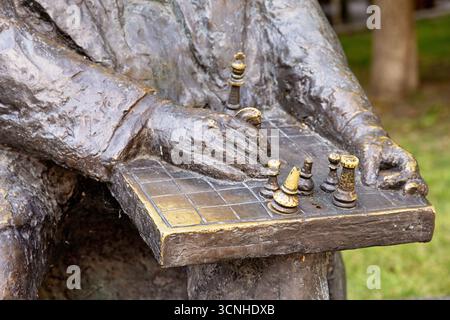 Primo piano di una statua di bronzo del giocatore di scacchi che fa una mossa strategica su una scacchiera, mostrando il gioco intellettuale Foto Stock