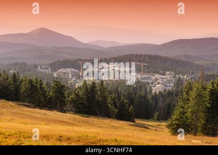 Gru che operano su un nuovo progetto alberghiero in una pittoresca località sciistica di Kopaonik, Serbia, illuminata da un vibrante cielo al tramonto Foto Stock