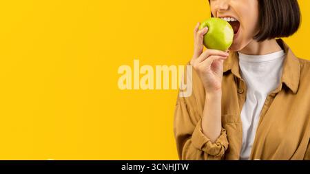 Concetto di stile di vita sano. Giovane donna che mangia gustosa mela su sfondo giallo, mordente frutta fresca deliziosa Foto Stock