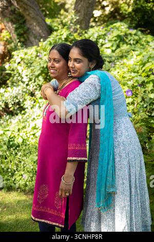 Madre e figlia indiane che abbracciano e sorridono nel cortile con indosso la tunica magenta e la dupatta Foto Stock