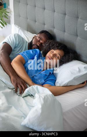 Coppie diverse sdraiate sul letto di casa con maglietta bianca pigiama blu sotto la testata grigia Foto Stock