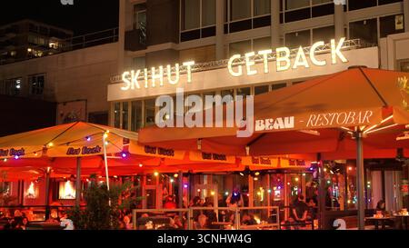 ROTTERDAM, PAESI BASSI - 13 SETTEMBRE 2025 - persone che si godono una terrazza bar all'aperto di notte a Rotterdam, Paesi Bassi, sotto luci colorate Foto Stock