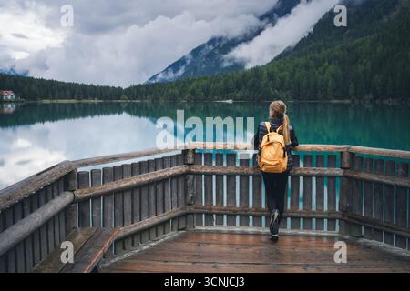 Donna con zaino giallo in piedi su una terrazza in legno vicino al lago Foto Stock