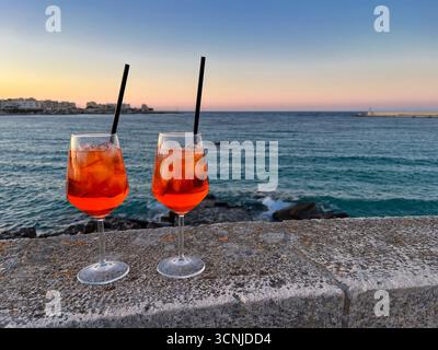 Due bicchieri di Aperol Spritz in riva al mare Adriatico di fronte all'orizzonte del tardo tramonto, Otrante, Italia Foto Stock