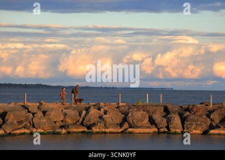 Irondequoit, NY, USA - 7 settembre 2025 - due uomini escono con il loro cane fedele all'alba per pescare da un molo nella parte settentrionale dello stato di New York Foto Stock