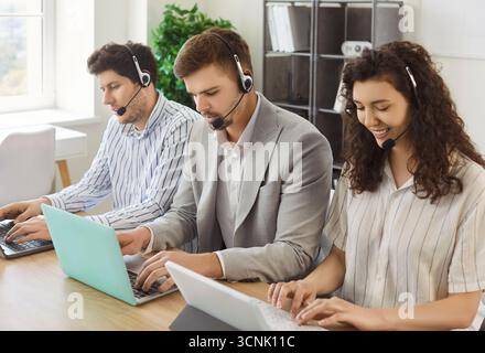 Giovani uomini d'affari seduti di fila che lavorano in call center presso l'ufficio del servizio di assistenza online. Foto Stock