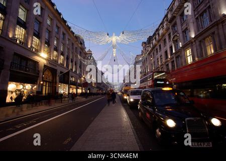 LONDRA, REGNO UNITO. 17 DICEMBRE 2016. Un taxi nero di Londra e un autobus rosso a due piani passano sotto le decorazioni degli angeli di Natale su Regent Street all'ora blu. Foto Stock