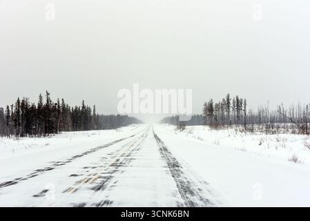 La MacKenzie Highway nei territori del nord-ovest in una giornata nevosa che dimostra una prospettiva in diminuzione Foto Stock
