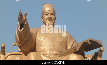 La statua in bronzo dorato del re Sejong il grande, che tiene un libro e gesta con una mano alzata, sotto un cielo azzurro limpido a Seoul, Corea del Sud. Foto Stock