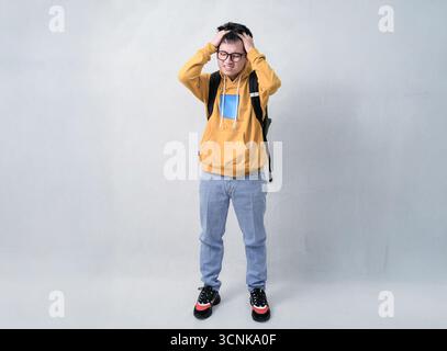 giovane uomo con cappuccio giallo e zaino che afferra la testa in un ritratto in studio di soccorso Foto Stock
