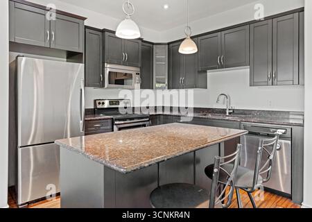 Cucina con frigorifero argentato, microonde e forno. Il bancone è realizzato in granito e ha un lavandino in argento. Ci sono due sedie in cucina Foto Stock