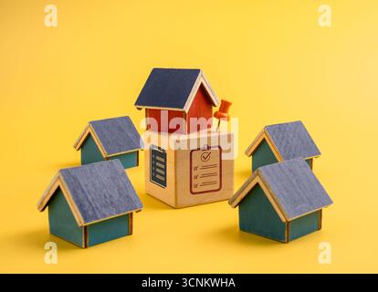 Modelli di case con blocco lista di controllo con perno su sfondo giallo che rappresenta la decisione di acquisto della casa, la valutazione del valore immobiliare, la scelta del mercato, il mutuo Foto Stock