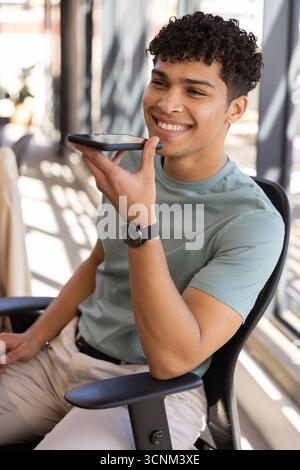 Uomo con orologio da polso in una sedia da ufficio accanto alla finestra che parla nello smartphone all'ombra della luce del sole Foto Stock