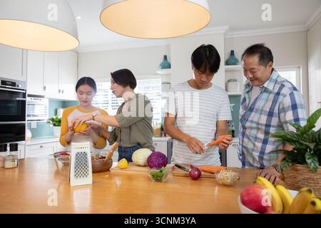Una famiglia di quattro persone che si trova intorno all'isola di cucina, affettando peperoni e pelando carote Foto Stock
