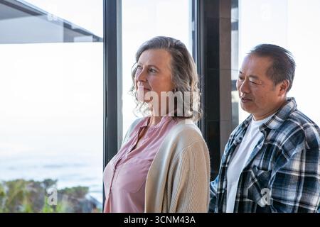 Diverse coppie anziane che osservano l'oceano attraverso la finestra all'interno della casa con piante costiere Foto Stock
