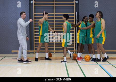 Allenatore maschile che insegna a squadre di basket diverse, accostandosi al campo con il basket Foto Stock