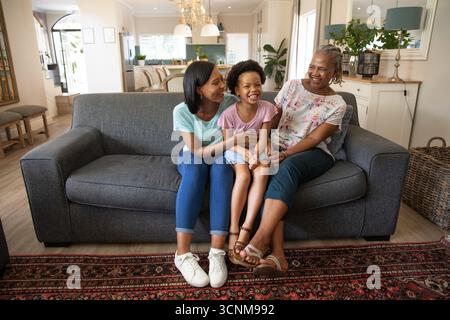 Diverse famiglie sedute su un divano grigio antracite nel soggiorno con tappeto e credenza a motivi geometrici Foto Stock