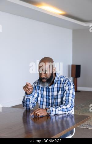 Uomo afroamericano seduto nell'area lounge al tavolo che punta a destra indossando un orologio da polso Foto Stock