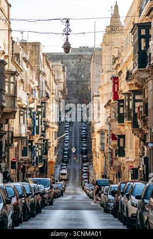 La Valletta, Malta - 11 aprile 2025: Ripida strada della città costeggiata da automobili e tradizionali balconi maltesi Foto Stock