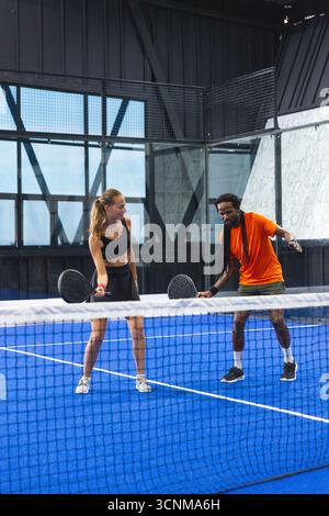 Diversi giocatori indossano abbigliamento sportivo che praticano il padel sul campo blu con racchette in rete bianca Foto Stock