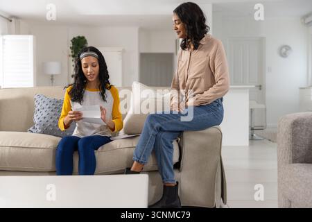 Leggendo lettere stampate, mamma e figlia adolescente diverse sedute sul divano di casa Foto Stock
