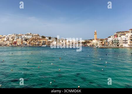 Vista panoramica sul lungomare di Marsaskala con edifici colorati, barche e acque turchesi limpide in un giorno di primavera soleggiato, Malta, Europa Foto Stock