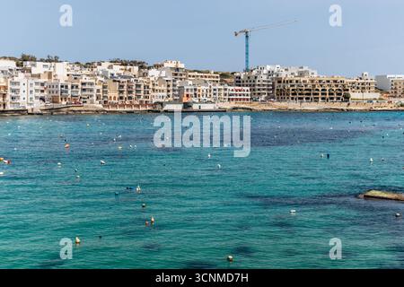 Vista panoramica sul lungomare di Marsaskala con edifici colorati, barche e acque turchesi limpide in un giorno di primavera soleggiato, Malta, Europa Foto Stock