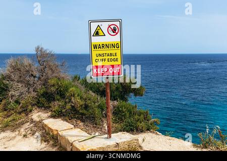 Percorso costiero tra Marsaskala e Marsaxlokk, Malta. Cartello segnaletico indicante l'instabilità della scogliera e il pericolo con vista sul Mar Mediterraneo Foto Stock