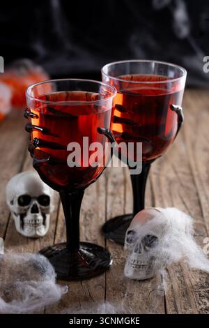 Spaventoso cocktail rosso di Halloween in vetro a mano sullo scheletro su un tavolo di legno Foto Stock