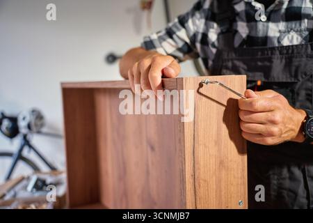 Primo piano del falegname con chiave a brugola durante l'assemblaggio di mobili in legno in officina. Uomo che utilizza una chiave esagonale per serrare le viti. Concetto di falegnameria e pelliccia Foto Stock