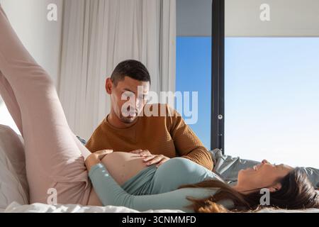 Diverse coppie che si aspettano di condividere momenti sdraiati sul letto nella moderna camera da letto tramite finestre scorrevoli in vetro Foto Stock