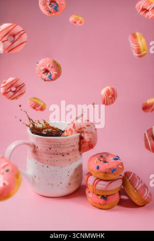 Ciambelle cadenti con caffè spruzzato su sfondo rosa Foto Stock