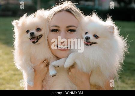 Donna sorridente che abbraccia due soffici Pomerani all'aperto Foto Stock