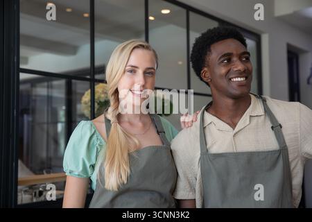 Diversi colleghi in piedi presso la caffetteria indossano grembiuli grigi vicino alla partizione in vetro e alla macchina per il caffè Foto Stock
