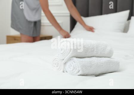 Cameriera che lavora in camera, concentratevi su una pila di asciugamani in spugna sul letto Foto Stock