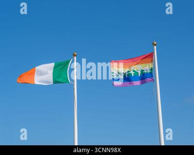 Irlanda e bandiera arcobaleno che sventolano su palafitte contro il cielo azzurro cristallino di West Cork. Foto Stock