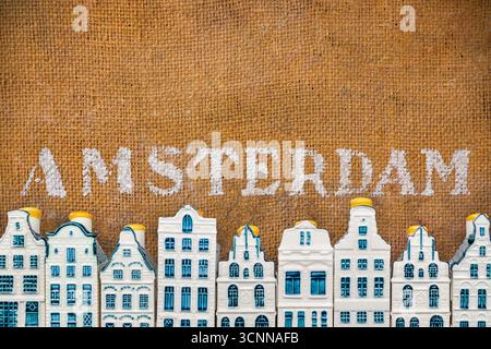 Fila di case in porcellana souvenir in miniatura blu davanti a un vecchio sfondo marrone con il testo Amsterdam Foto Stock
