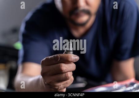 Uomo che ripara il motore di un'auto e tiene in mano una candela difettosa, concetto di riparazione auto, manutenzione auto e lavori meccanici. Foto Stock