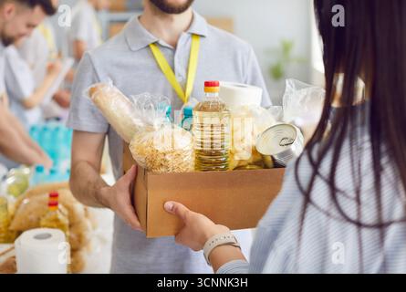 Un uomo volontario in un magazzino dà a una donna una scatola di cibo, da vicino Foto Stock